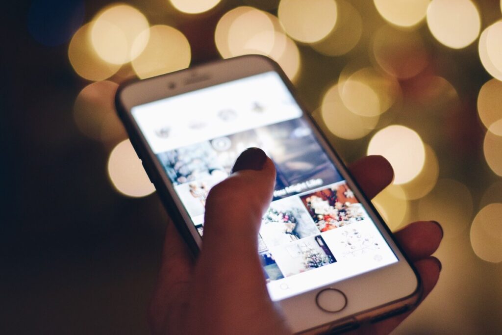 Woman holding iPhone looking at wedding ideas on Instagram. Fairy light bokeh background.