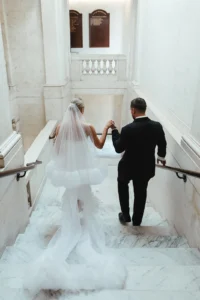 Chic city bride in an elegant modern gown walking down the stairs with her groom