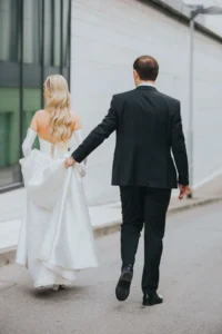 Bride with elegant soft waves walking hand in hand with the groom after wedding preparations