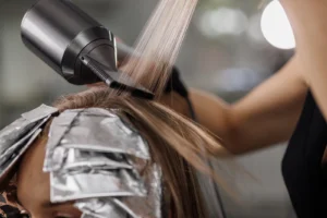 Hairdresser blow-drying freshly coloured hair with foil highlights