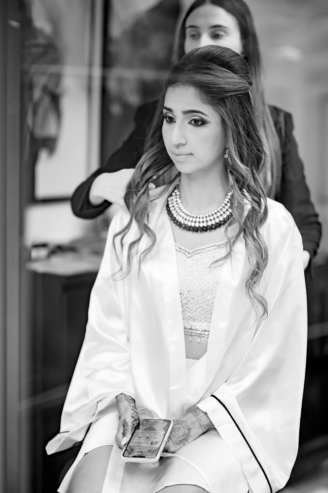 Bride getting her hair styled before the ceremony, wearing a silk robe and statement necklace