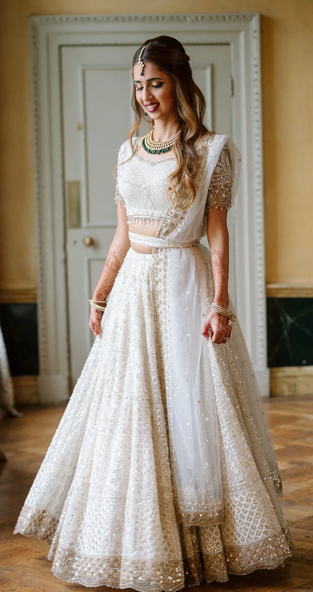Bride in an elegant white embellished lehenga smiling indoors before the ceremony