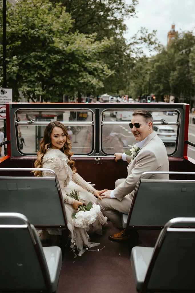 Bride Dannah and groom David holding hands on a classic London bus.