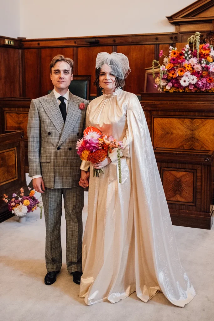 Bride Camilla and groom posing with a vibrant bouquet in London wedding hall