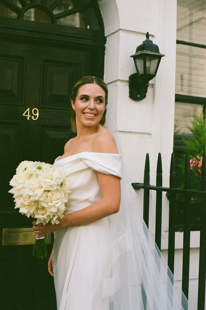 Bride smiling at the camera with her bouquet in front of a London residence