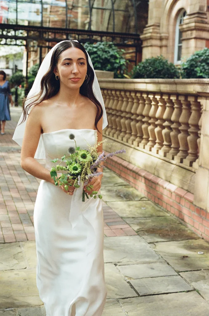 Bride walking down a historic London street with a bouquet of wildflowers.