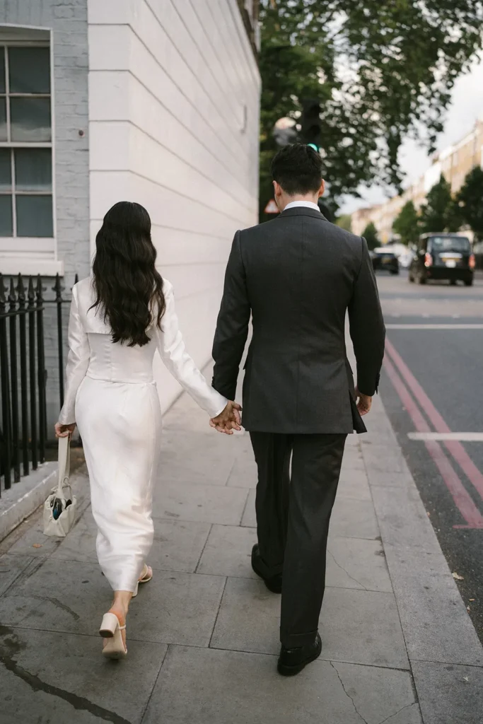 Bride and groom walking hand in hand along a London street, post-wedding.