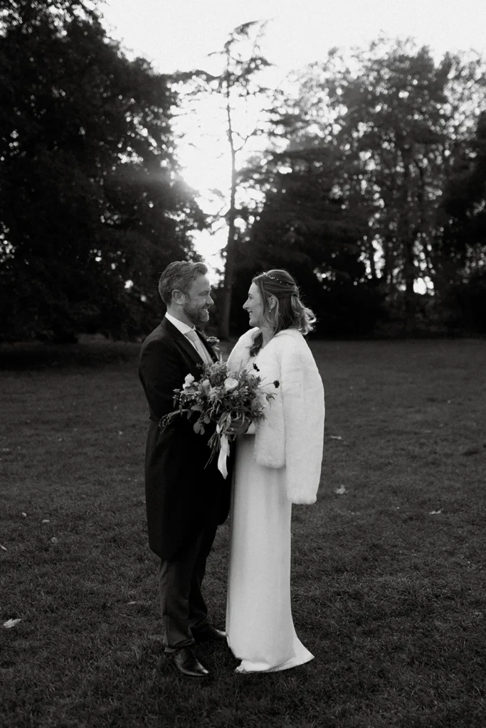 Bride and Groom standing in the garden at Fulham Palace London, gazing lovingly at each other as the sun sets behind them, highlighting the serene atmosphere.