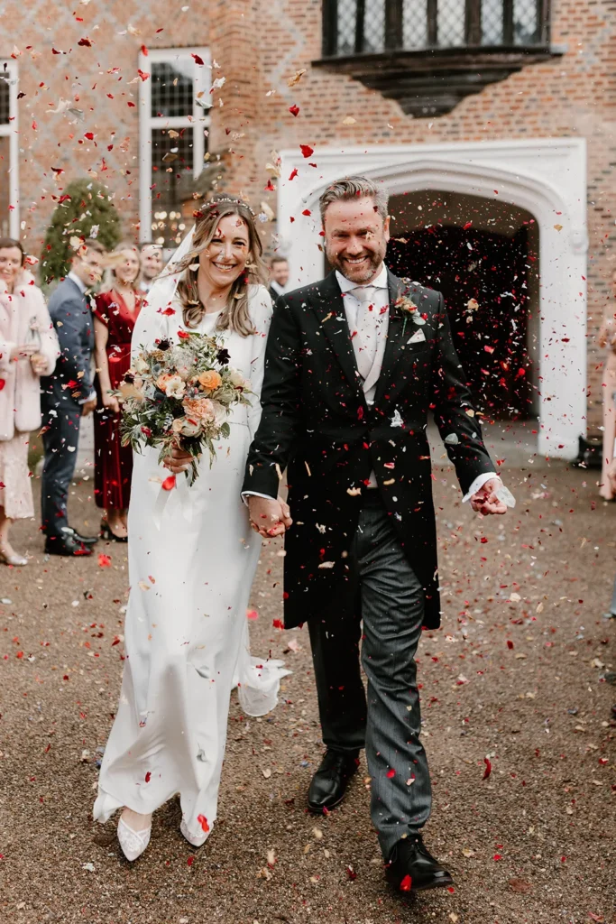 Bride and Groom being showered with confetti by their guests as they leave their wedding ceremony at Fulham Palace London, both beaming with happiness.