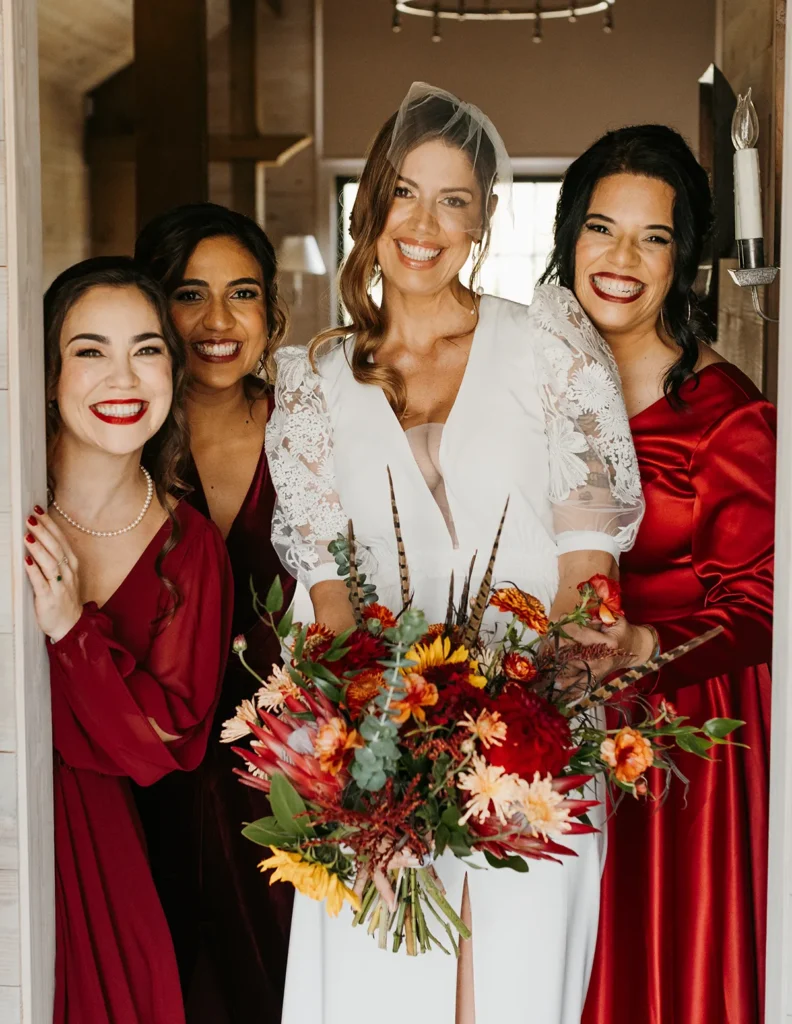 Bride surrounded by bridesmaids in red dresses, holding a bright bouquet