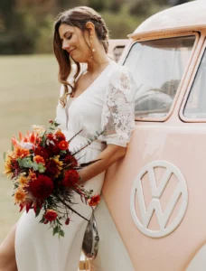 Bride leaning against vintage VW van holding a colourful bouquet