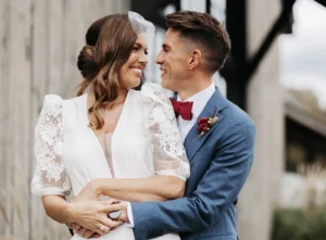 Bride and groom embracing in front of rustic wedding venue