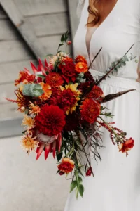 Bride holding vibrant boho chic bouquet with red and orange flowers