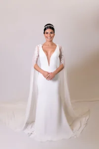 Elegant bride in a plunging white gown with sheer floral sleeves and a regal cape