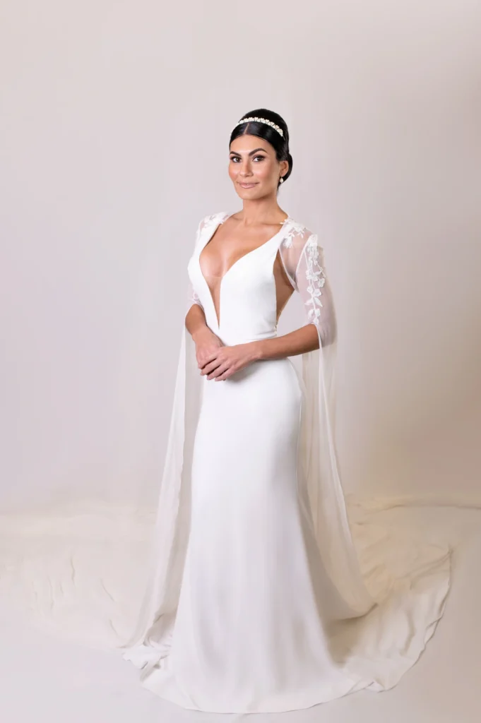 Full-length shot of bride in deep V-neck gown with floral lace details and cape sleeves