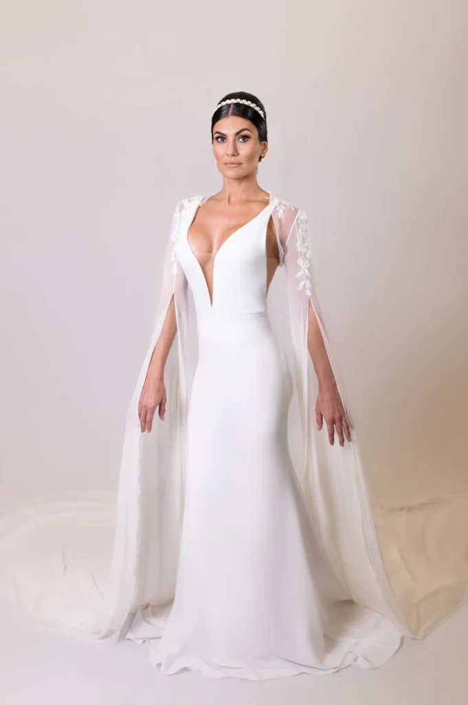 Bride in a sleek white gown holding her cape, showcasing intricate lace details