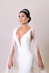 Bride posing confidently in a plunging gown with sheer embroidered sleeves and cape