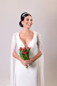 Bride holding a bouquet of red tulips in a white gown with a happy expression