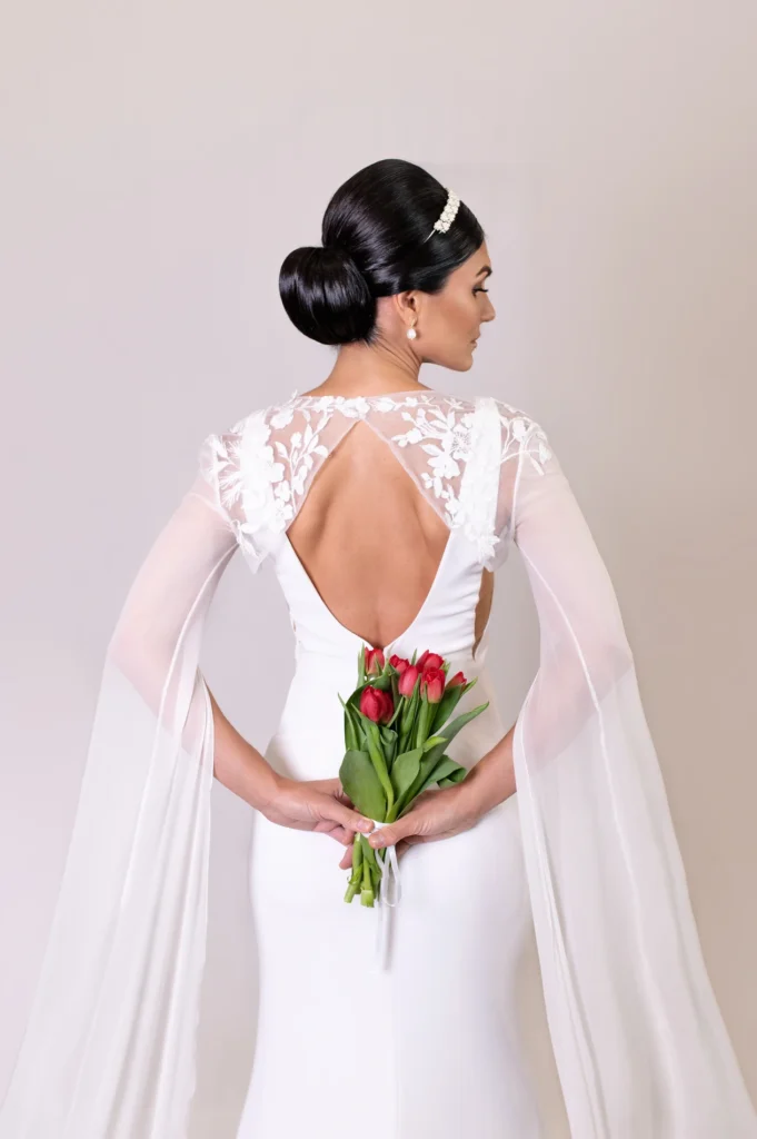 Bride looking down gracefully in a wedding gown with delicate sheer sleeves and cape