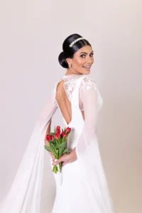 Smiling bride with a floral back detail on her gown, holding tulips behind her back