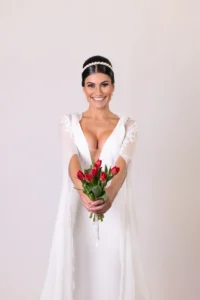 Smiling bride in a plunging wedding gown holding a bouquet of red tulips