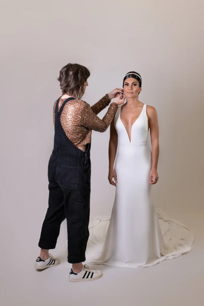 Behind-the-scenes shot of stylist adjusting the bride’s earrings in a white gown