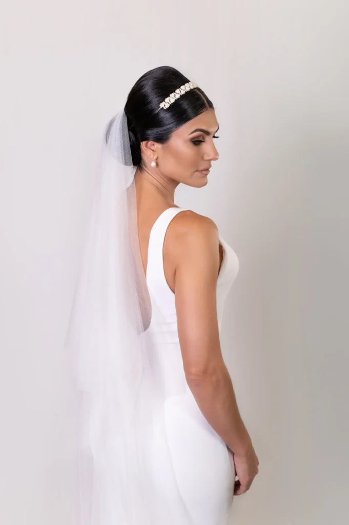 Side profile of bride with sleek hair, a pearl headband, and veil