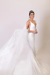 Bride in a sleek white gown with flowing veil, smiling elegantly for the camera