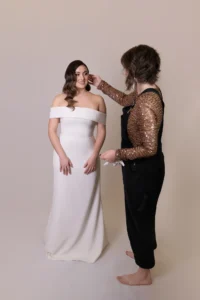 Stylist adjusts the hair of a bride in an off-the-shoulder wedding gown during photoshoot