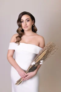 Bride in a minimalist off-shoulder wedding dress holding a rustic bouquet of dried flowers