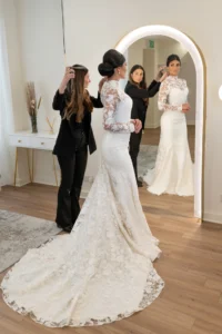 Hairstylist applying final touches to the bride's hair in a long lace gown