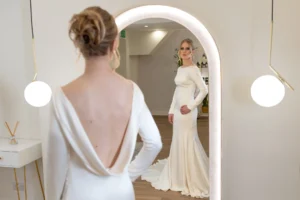 Bride admiring her gown in a mirror, showcasing a low back dress and updo hairstyle