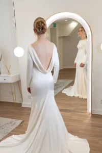 Bride in an open-back wedding gown looking at her reflection in a full-length mirror