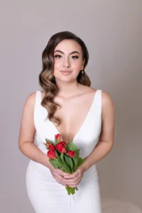 Bride in deep V-neck gown holding red tulips, soft makeup look