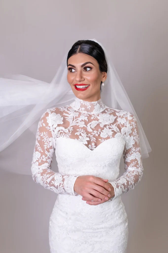 Bride in high-neck lace gown with vibrant red lipstick and flowing veil