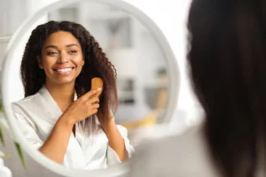 Smiling woman brushing her natural curly hair in front of a mirror.