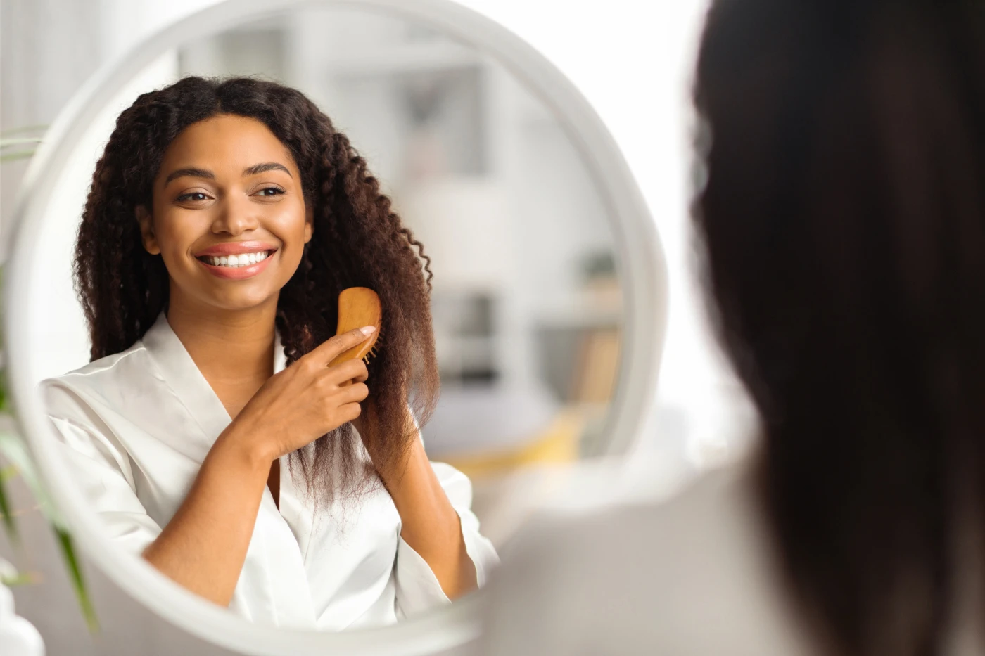 Smiling woman brushing her natural curly hair in front of a mirror.