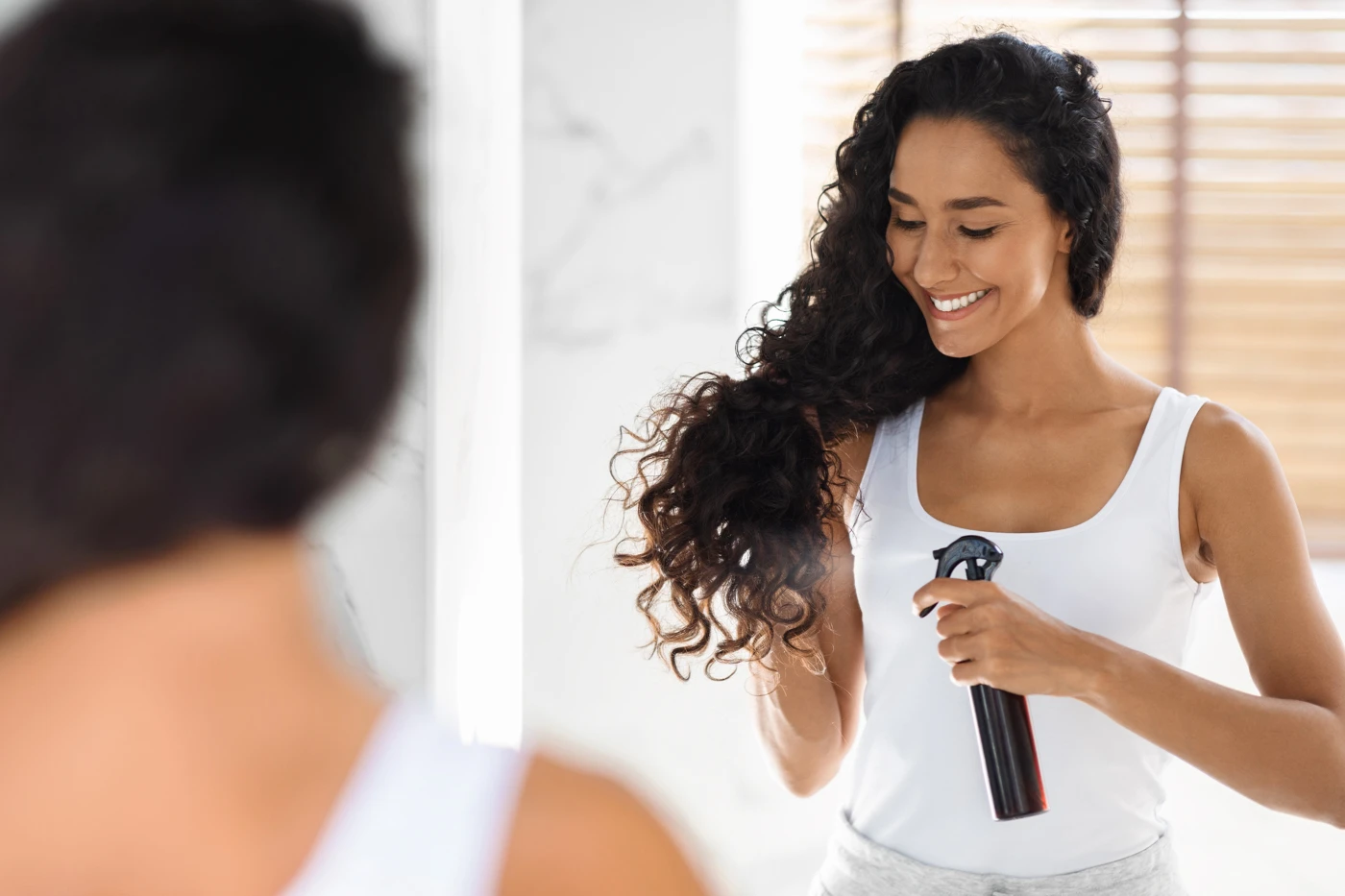 Woman spraying her curly hair with a hydrating mist.