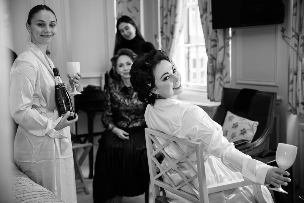 Bride getting ready with bridesmaids holding champagne in a cozy winter-themed bridal suite.