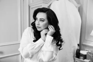 Bride fixing her earrings with soft curls in a romantic winter bridal suite.