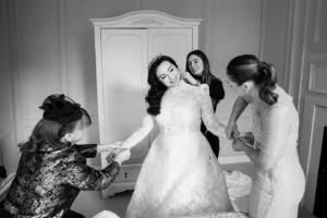 Bride in a lace gown assisted by bridesmaids in a winter-themed bridal suite.