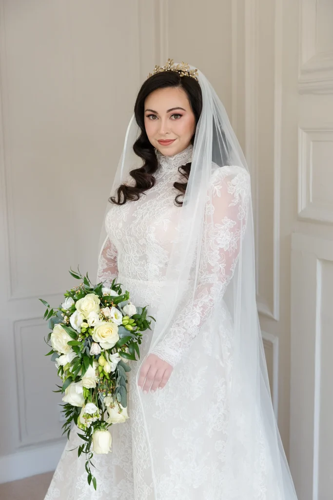 Winter bride in a lace gown and veil holding a cascading bouquet.