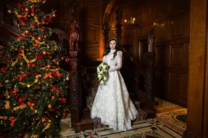 Bride posing beside a grand Christmas tree inside a historic venue, showcasing festive elegance.