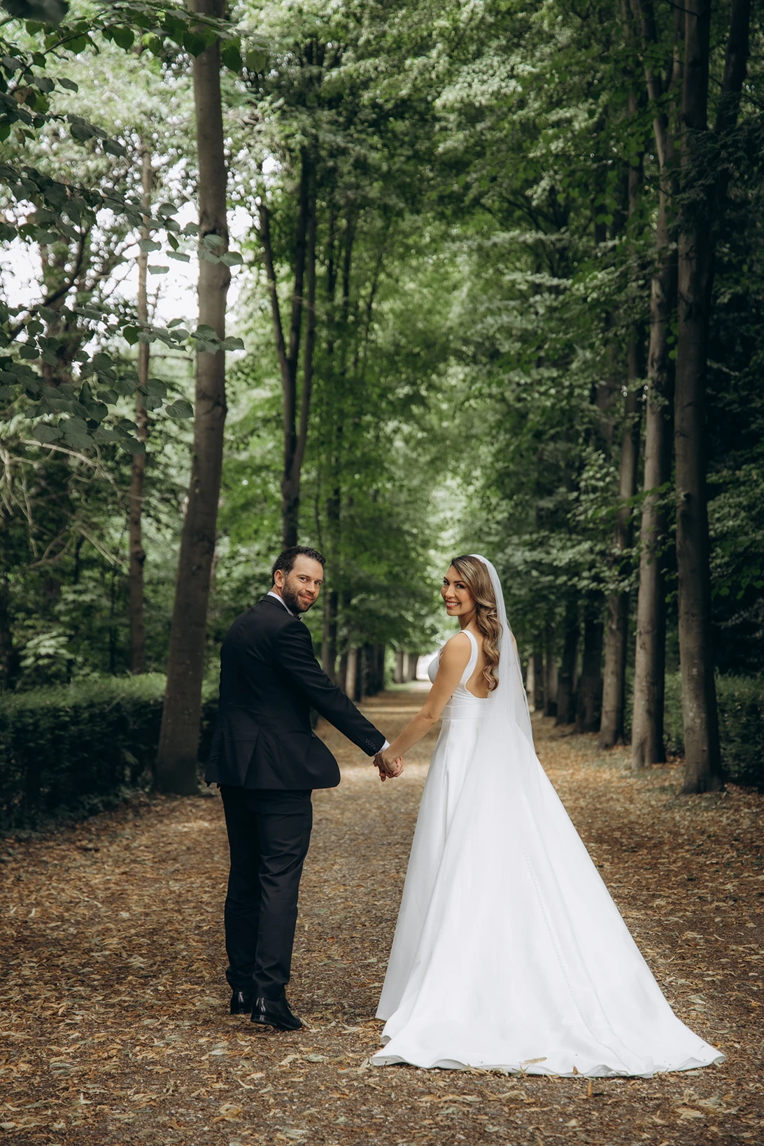 Bride and groom holding hands, walking down a tree-lined path