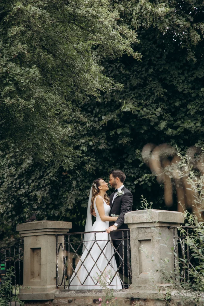 Bride and groom embracing on a historic bridge surrounded by greenery