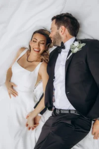 Bride and groom lying on a white backdrop, sharing a joyful moment