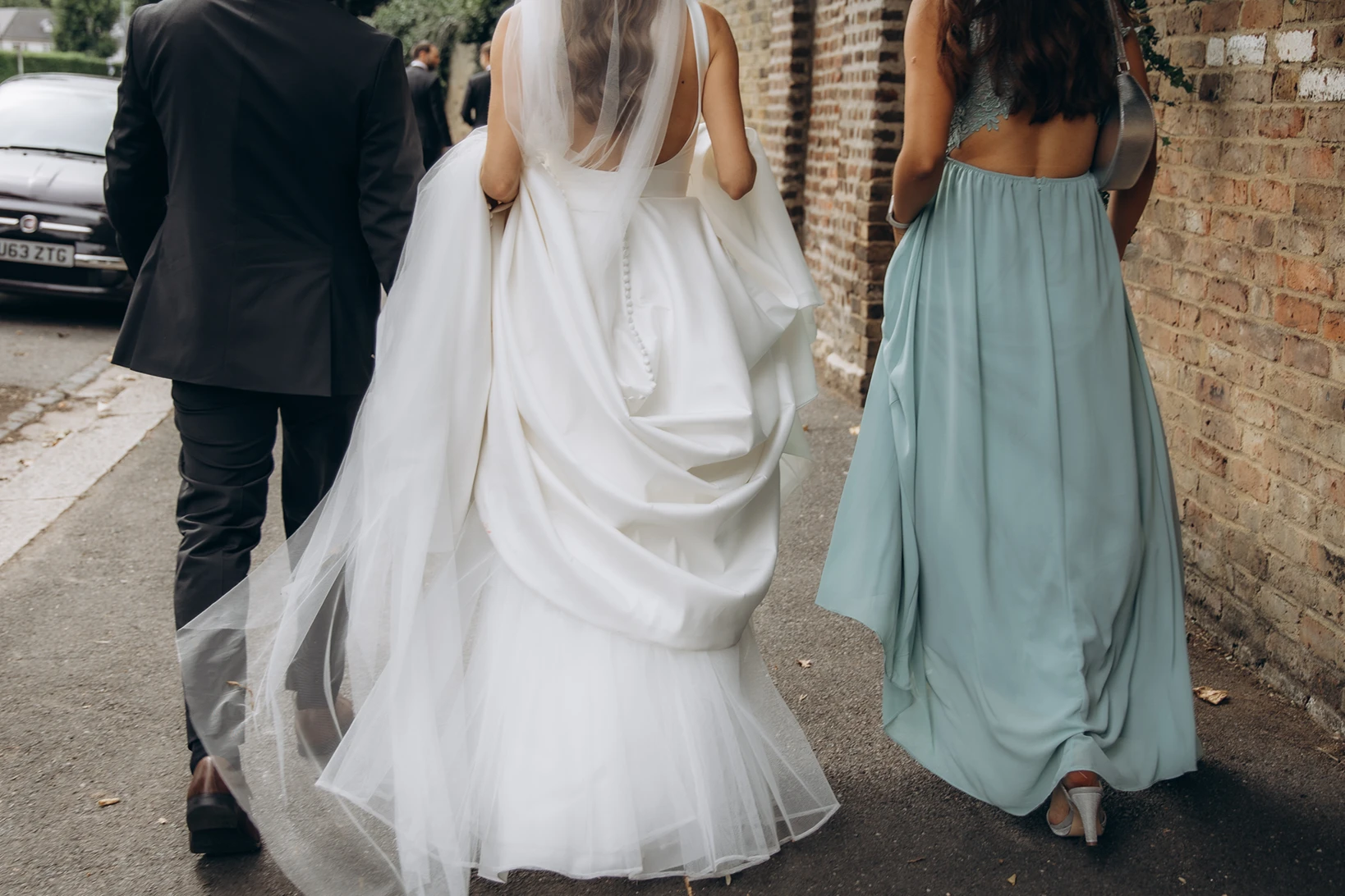 Bride walking alongside bridesmaid and groom, showcasing the elegant wedding gown.