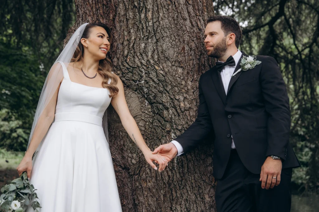 Close-up of the bride and groom holding hands against a tree during their wedding