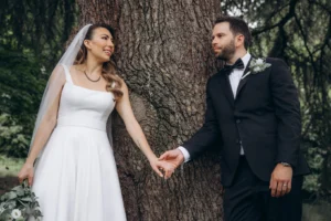 Close-up of the bride and groom holding hands against a tree during their wedding