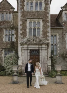 Bride and groom holding hands in front of the Loseley Park manor.